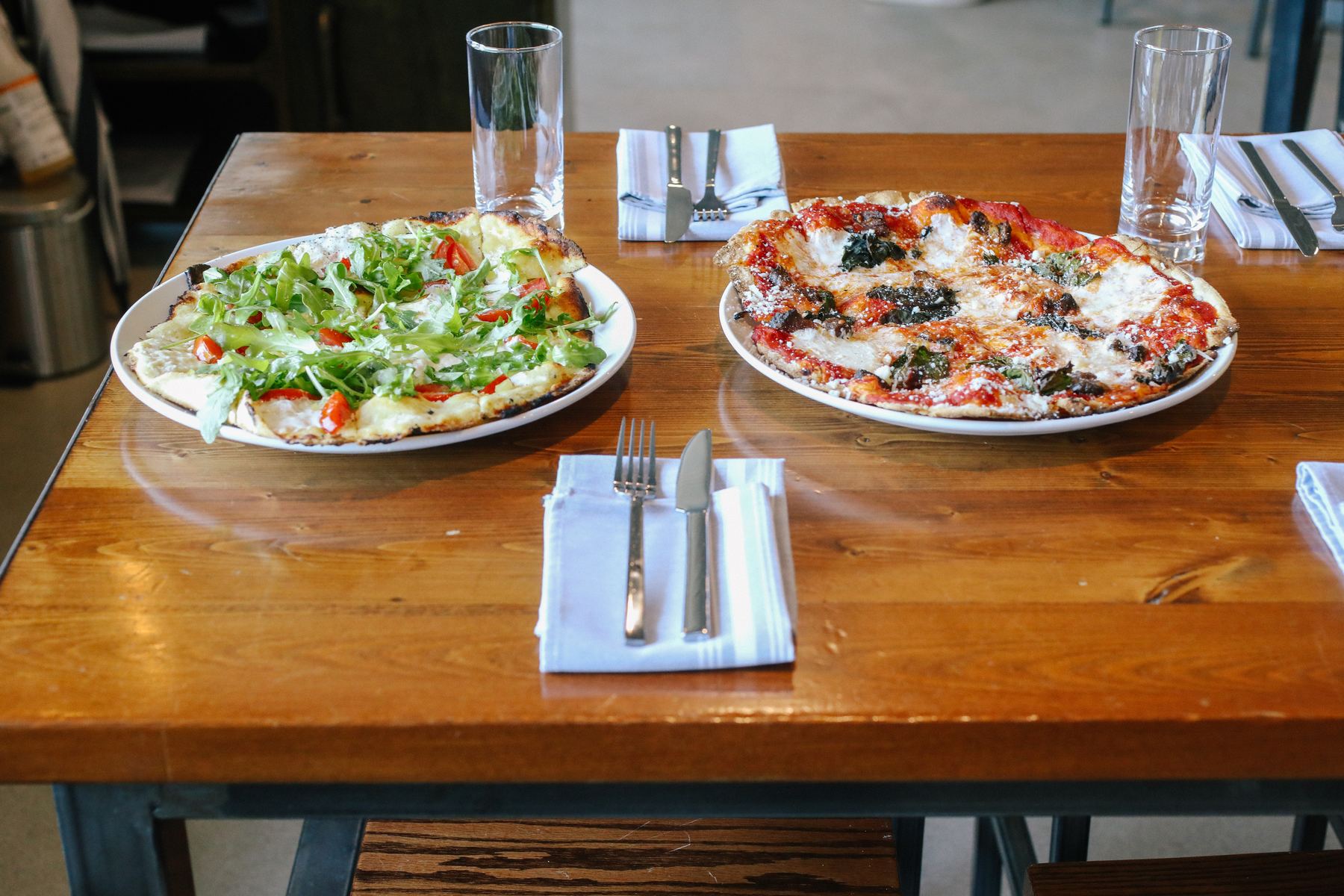 Two Amici pizzas served on a wooden dining table
